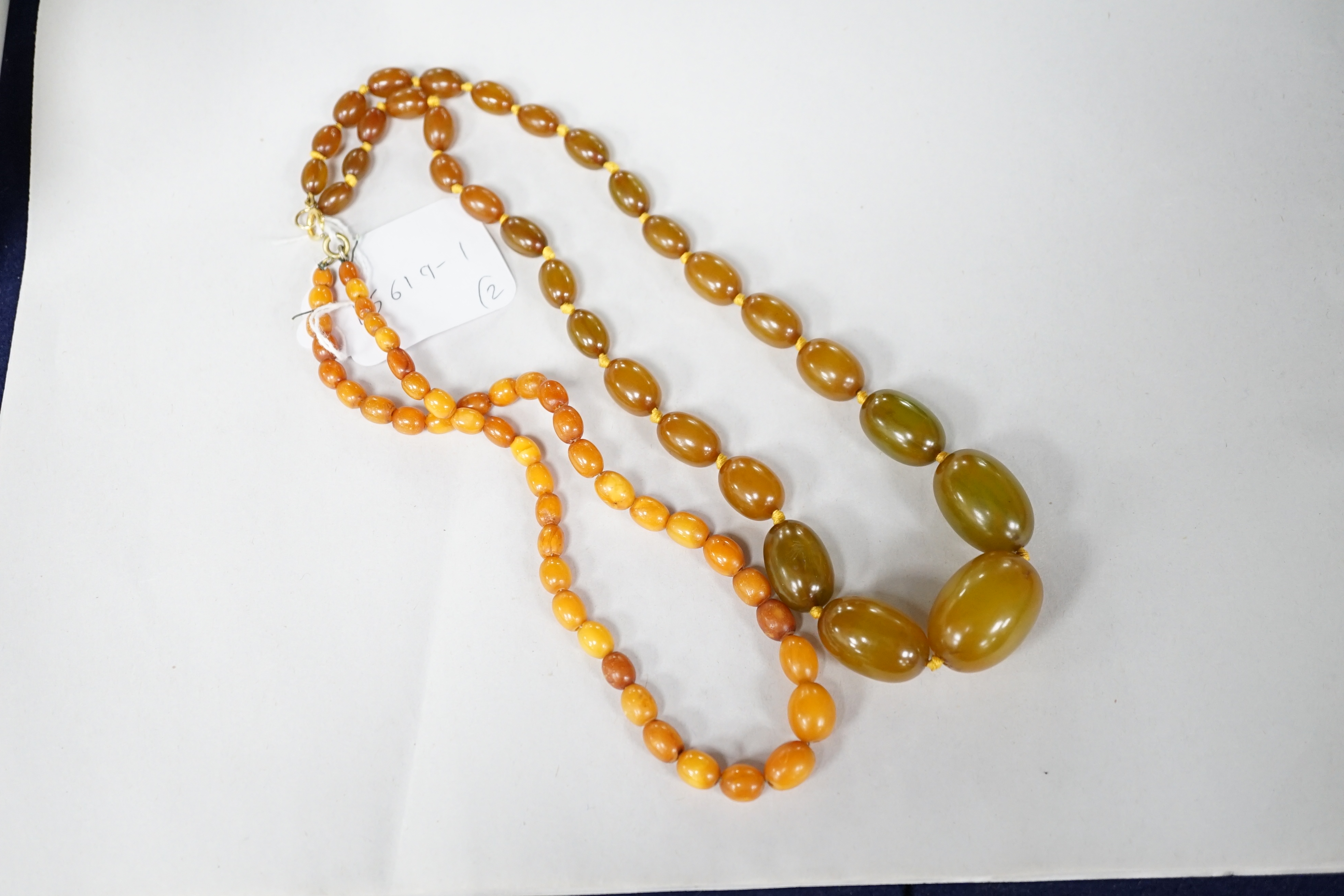 A small single strand graduated oval amber bead necklace, 40cm, gross weight 13 grams, together with a single strand graduated simulated green amber oval bead necklace, 54cm, gross weight 55 grams. Condition - poor to fa